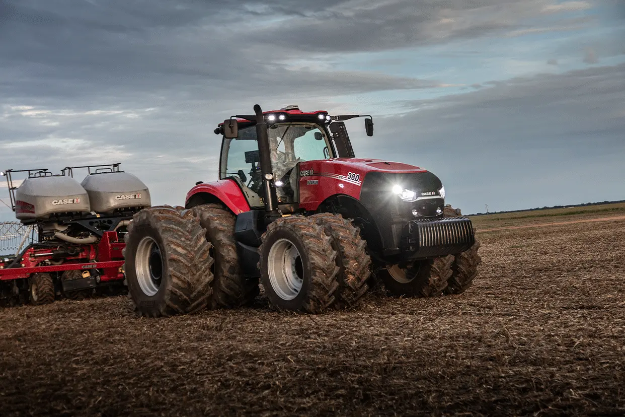 trator_magnum_em_campo_visto_lateralmente_a_direita_com_farois_acesos_em_aclive